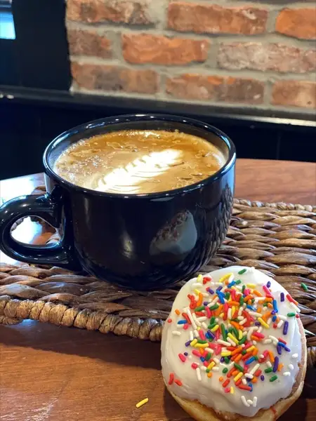 Latte in a blue mug beside a sprinkle doughnut