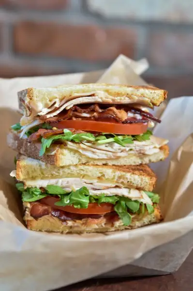 Stacked turkey and bacon sandwich with a drink and salad