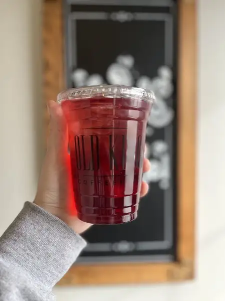 Iced hibiscus tea held in front of the drink chalkboard
